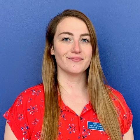 Ali Ross stands smiling against a blue background